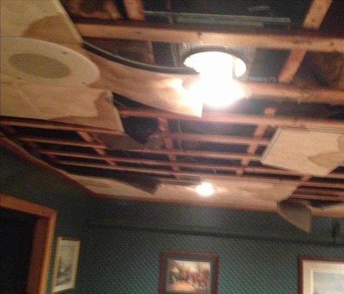 A basement ceiling with damaged and missing ceiling tiles due to an upstairs pipe break